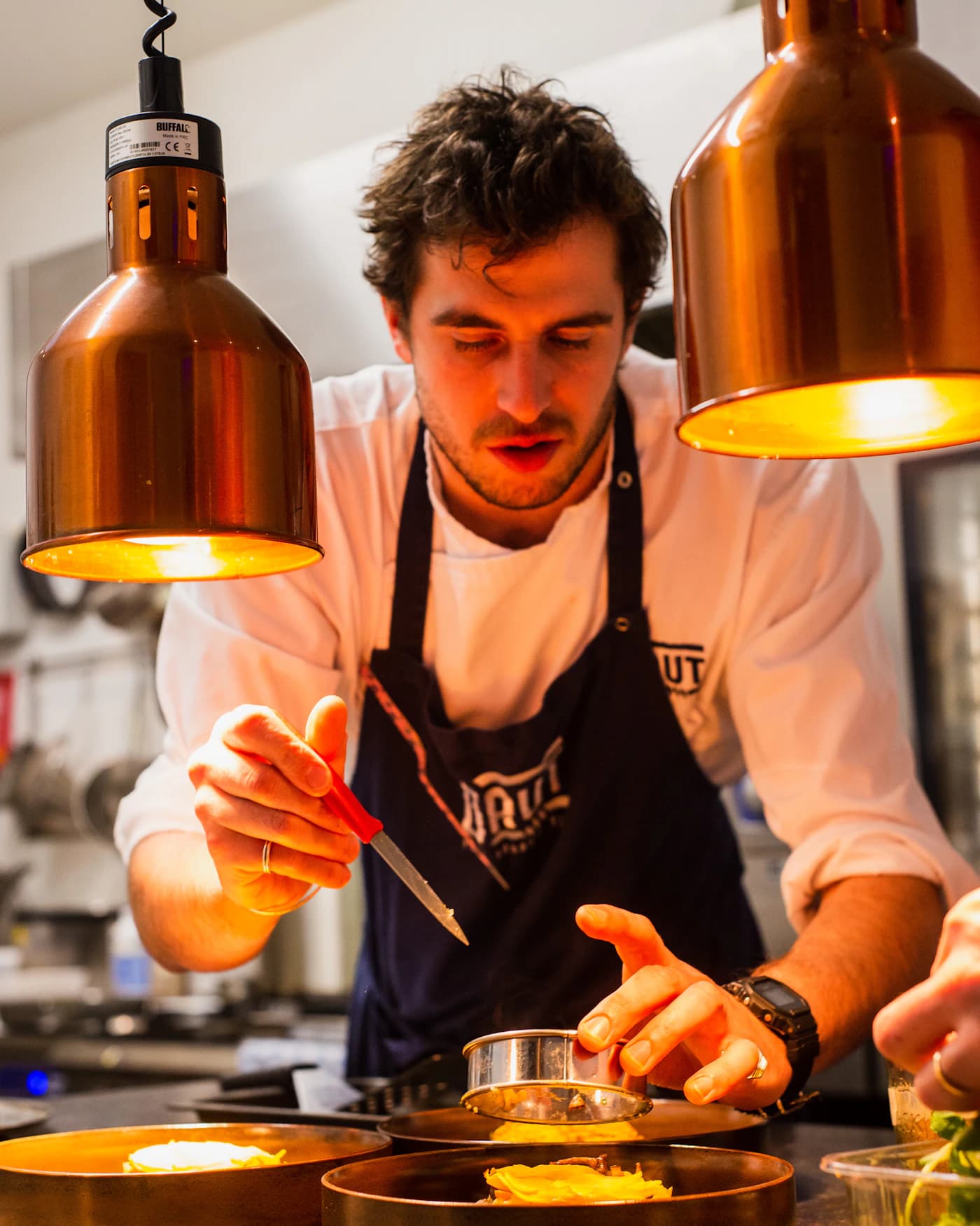 Chef carefully plating a dish under warm kitchen lights.