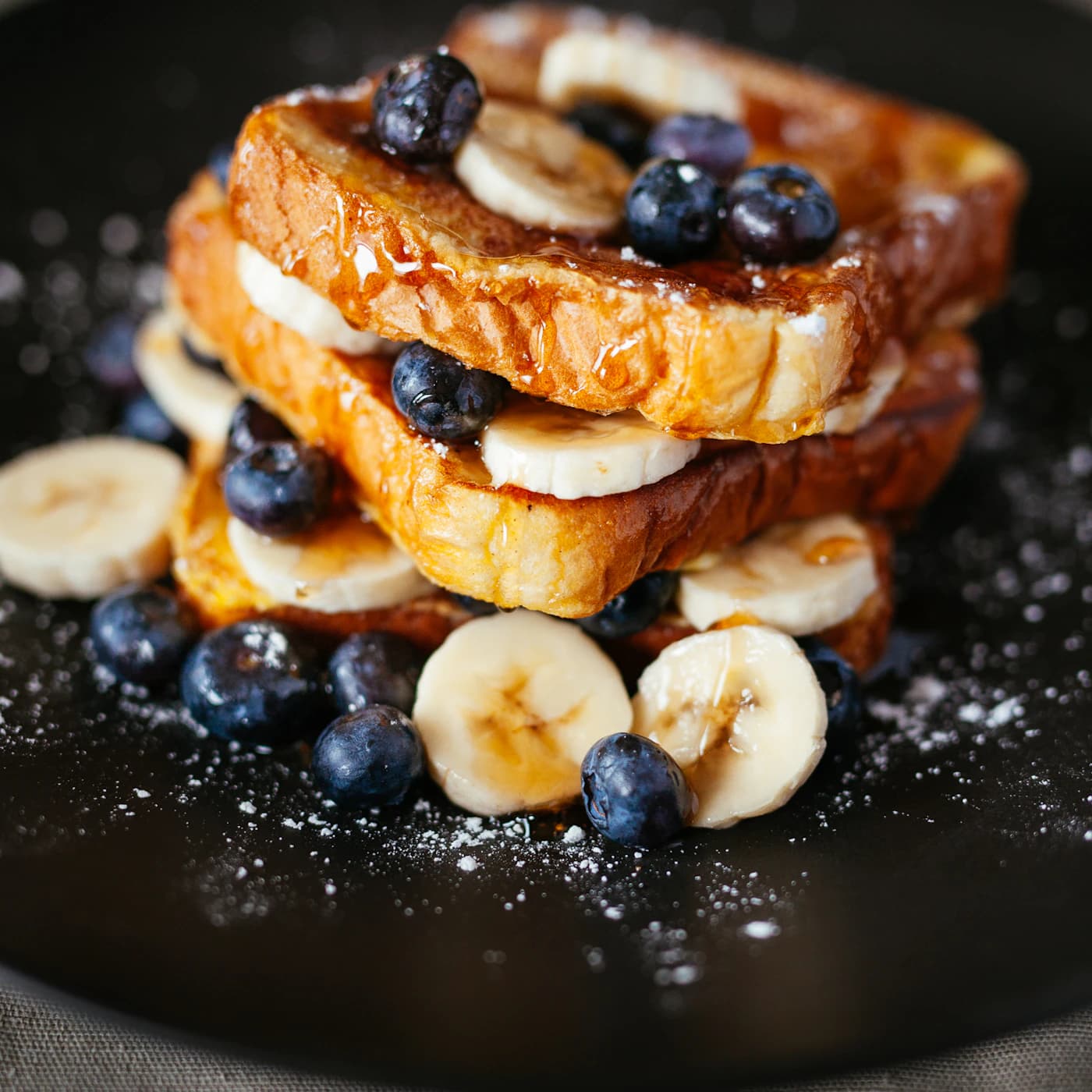 Stack of French toast with banana slices and blueberries.