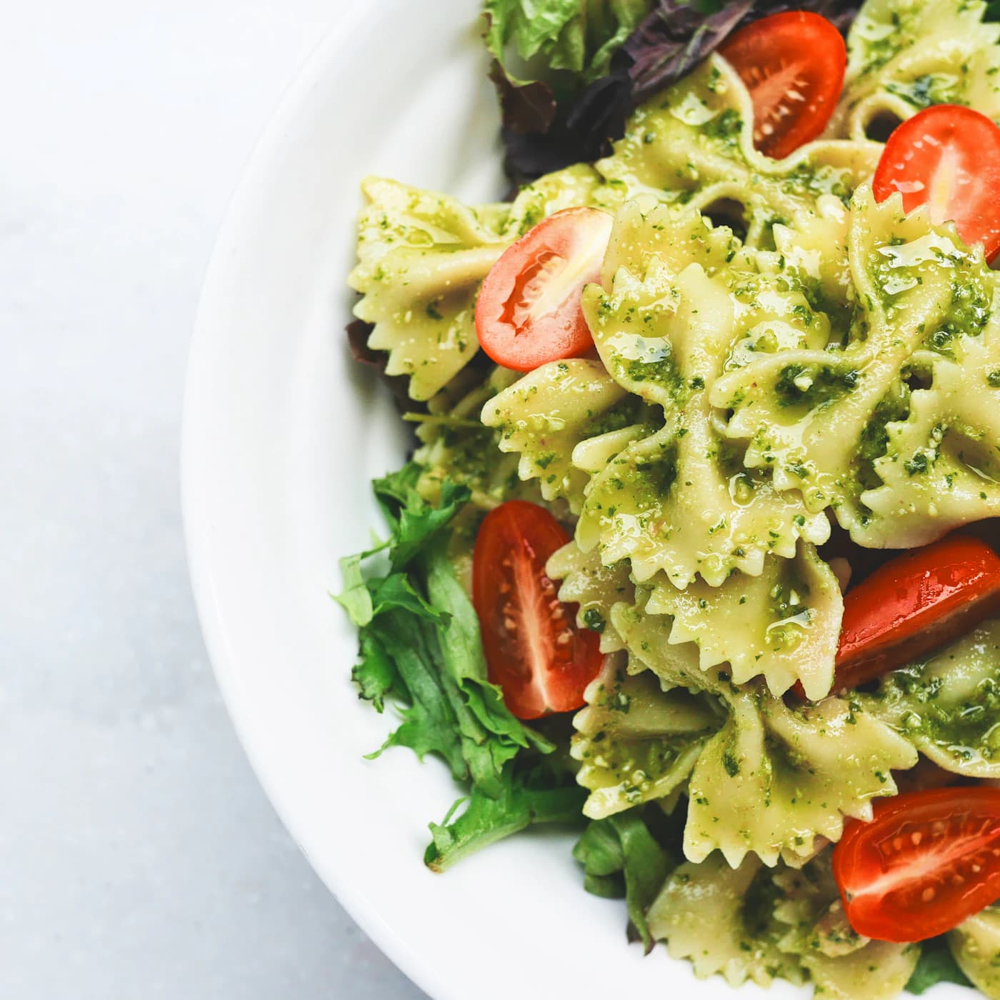Bowtie pasta in pesto with cherry tomatoes and greens.