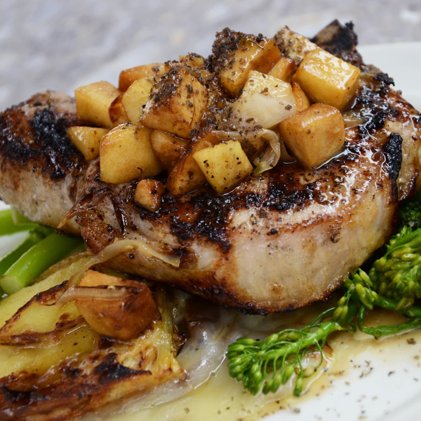 Grilled pork chop topped with roasted potatoes and broccolini.