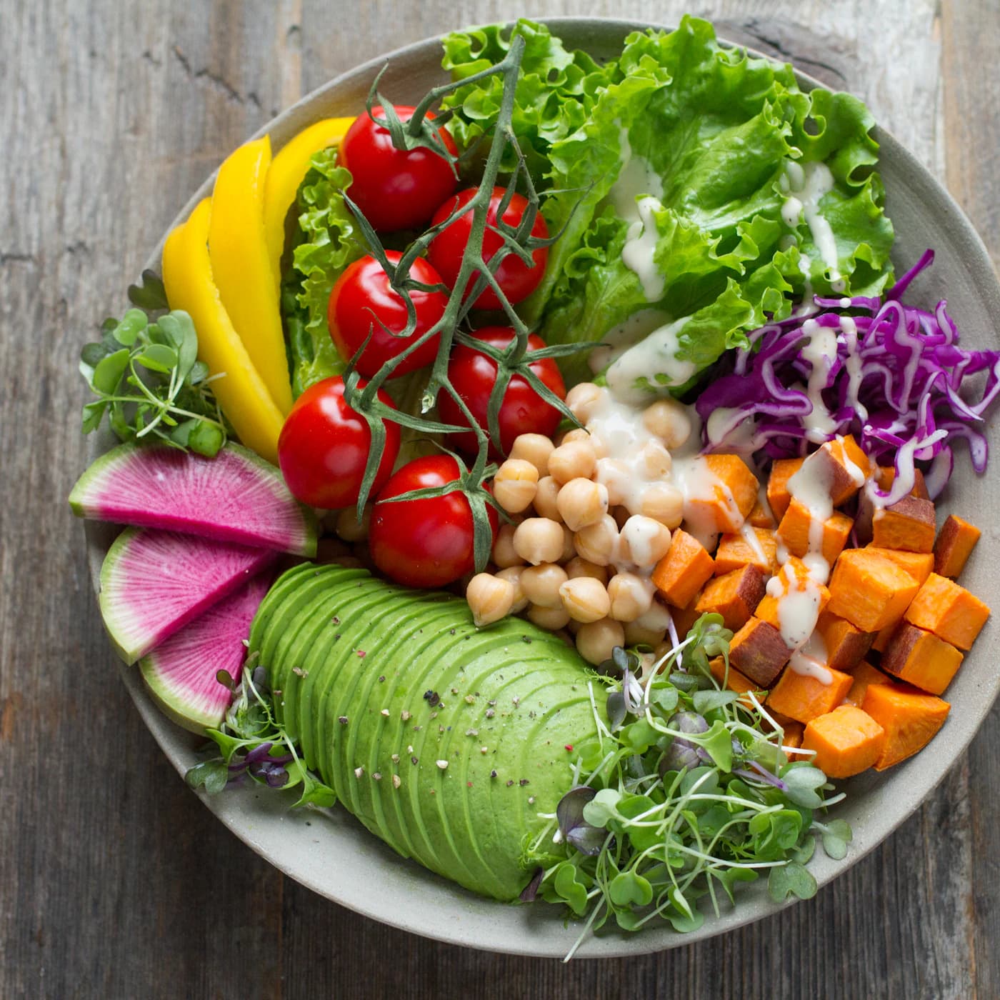 Plate of avocado, chickpeas, roasted sweet potato, tomatoes and purple cabbage.