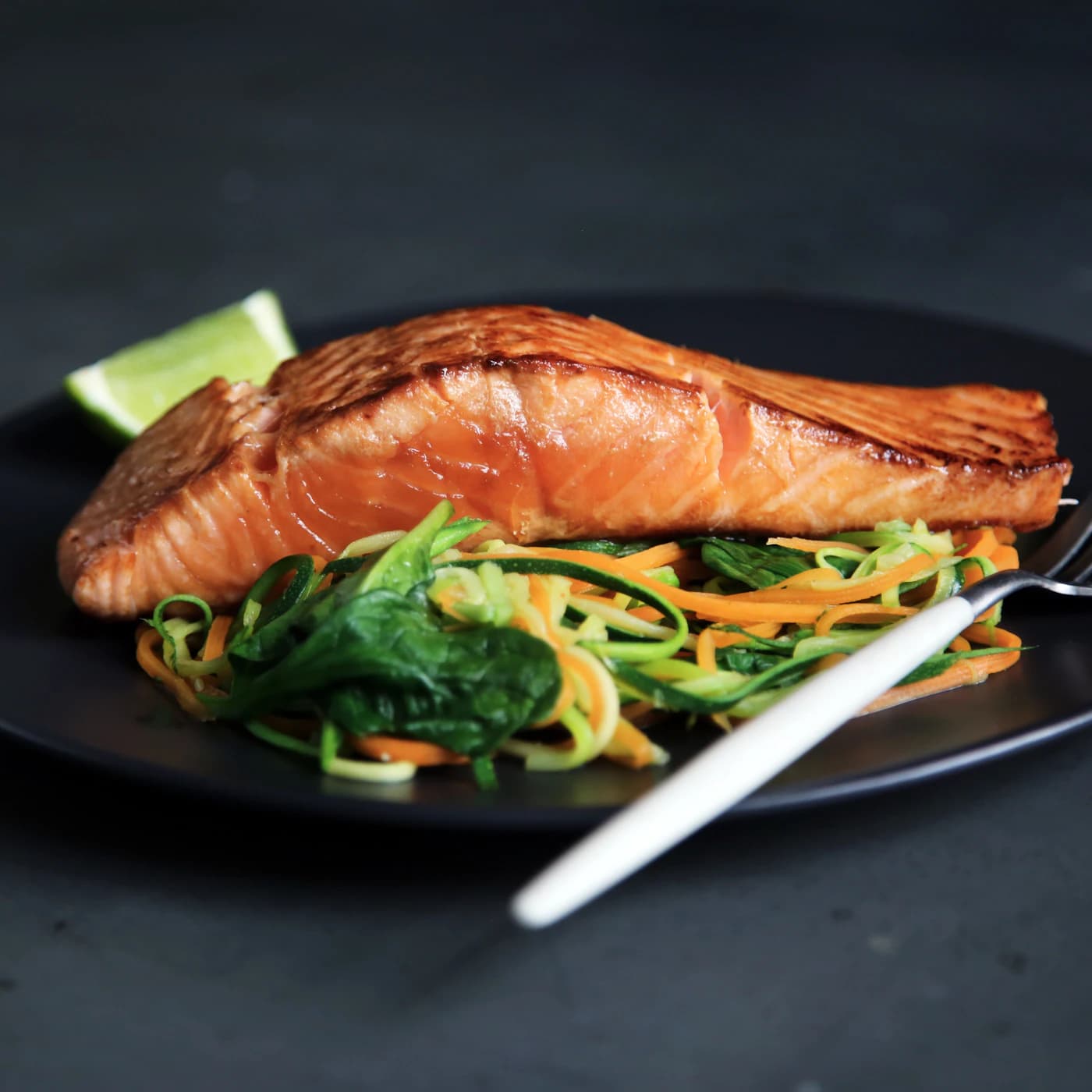 Crispy-skin salmon fillet over sautéed greens on a dark plate.