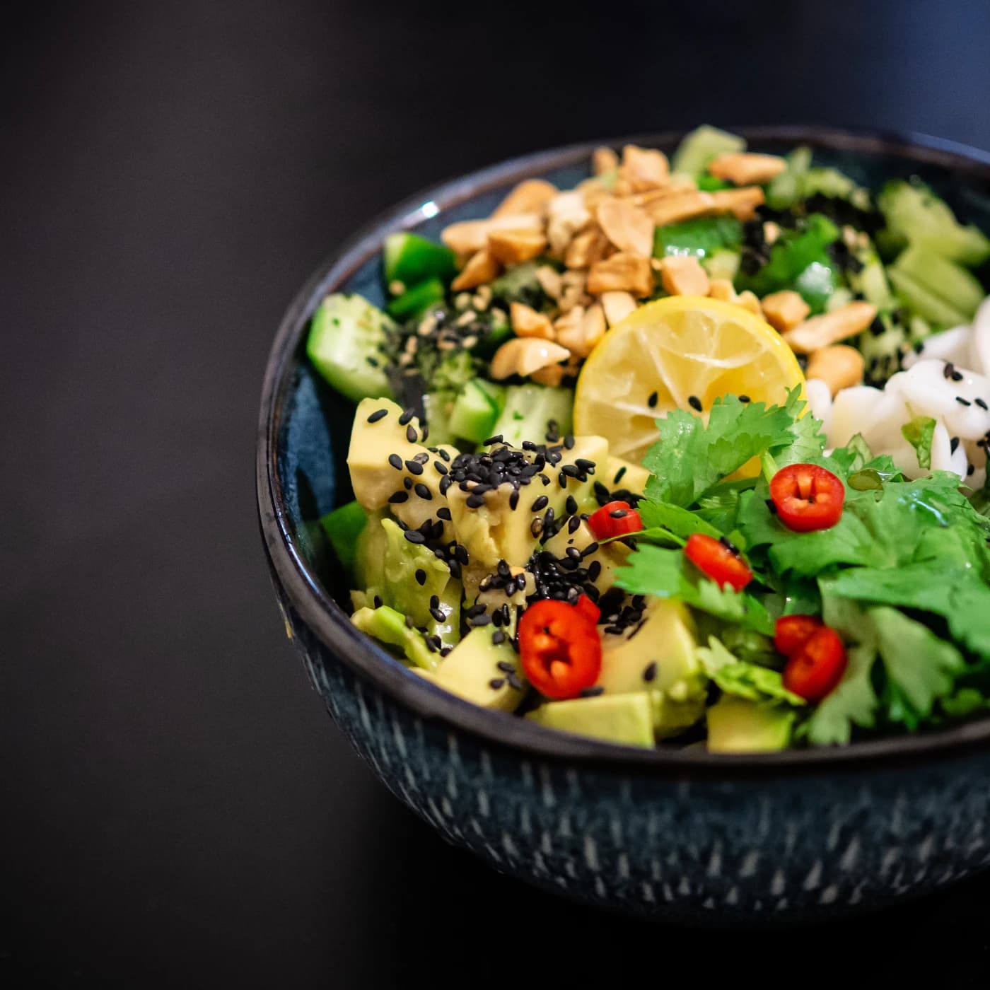 Dark bowl of chopped salad with avocado, cucumber, peanuts and sesame.
